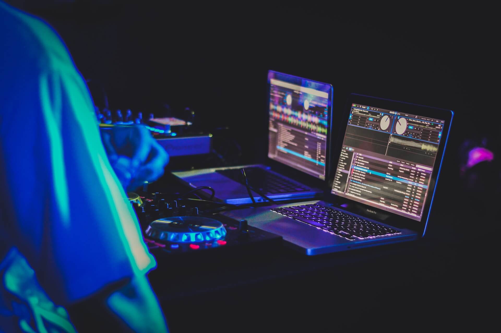 Two laptop computers displaying music software and DJ turntables.